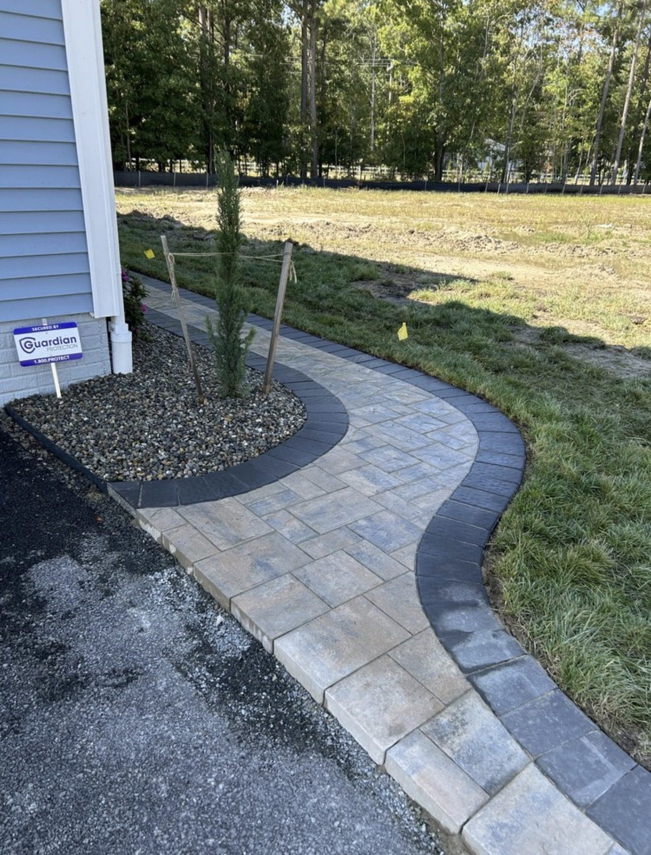 Curved light paver walkway with a dark border beside a home and planting bed