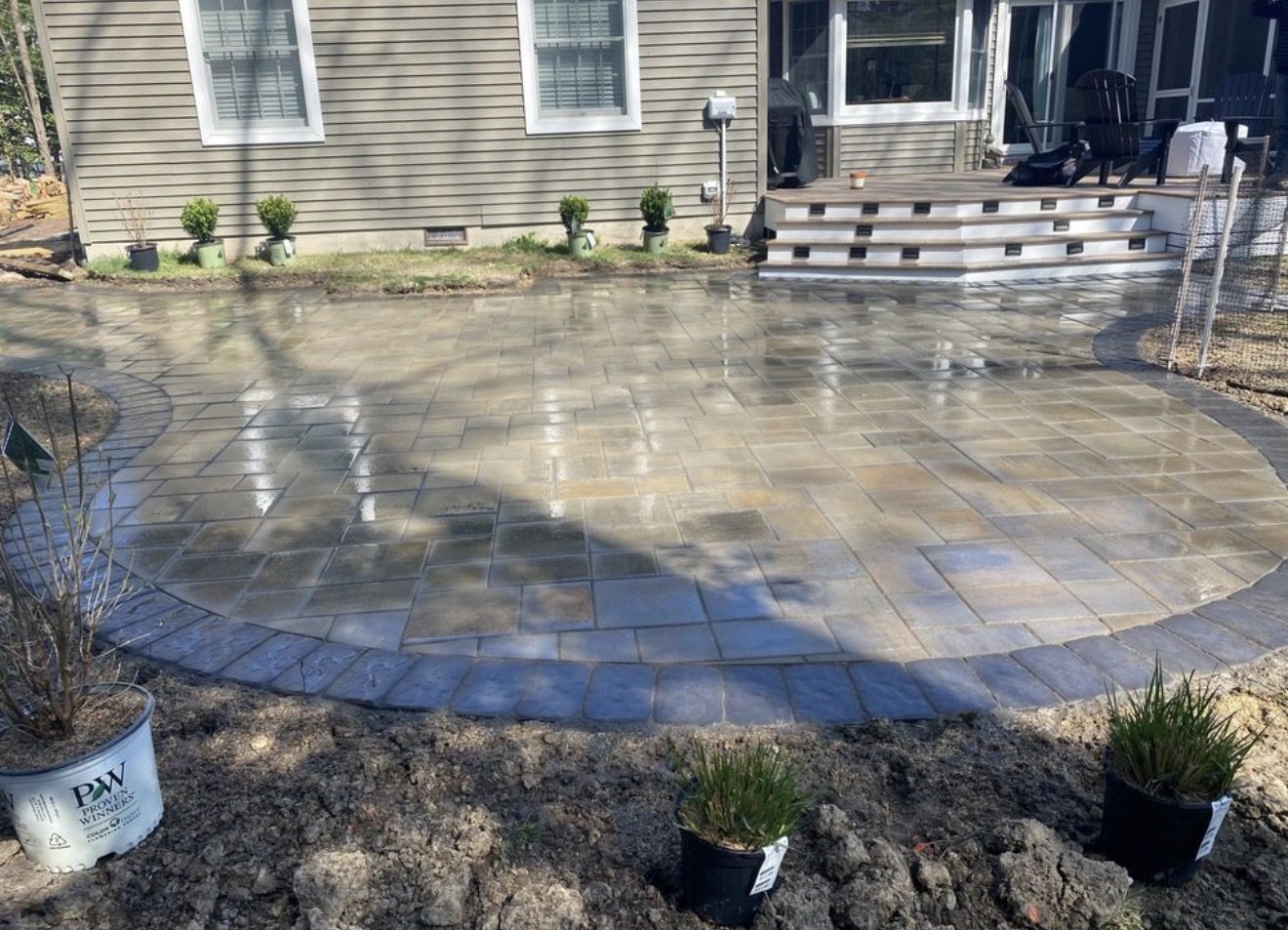 Paver patio with a curved dark border in front of a home and deck steps